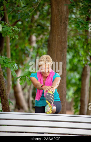 Donna senior con asciugamano attorno al collo esercizio di stretching riscaldamento fino all'aperto in una foresta Foto Stock