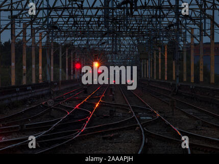 Vista guardando verso nord lungo il binario 4 west coast mainline sul viadotto di Stockport al tramonto con il rosso e il giallo glinting segnali sulla traccia del lavoro Foto Stock