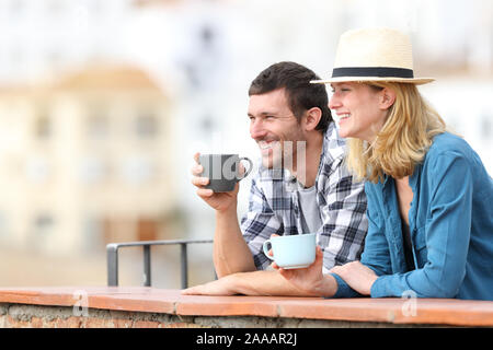 Felice coppia di turisti a bere caffè e guardando lontano in un balcone in un borgo rurale in vacanza Foto Stock