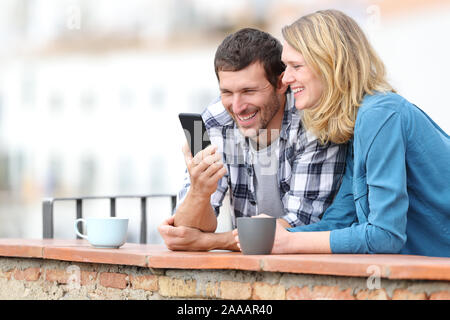 Adulto felice coppia controllo smart phone in piedi all'aperto in un balcone in un paese rurale Foto Stock