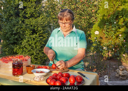 Donna tagliare i pomodori, nel giardino in estate e al tramonto Foto Stock