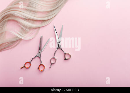 Forbici e altri parrucchiere accessori e trefolo di capelli biondi su sfondo rosa. Lay piatto con spazio per il testo. Parrucchiere Servizio. Bellezza Foto Stock