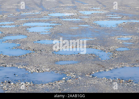 Sole sul parcheggio hardcore con pozze d'acqua in piedi in cavità / pozze tuffi. Cielo blu riflesso in pozze, riflessi acqua. Foto Stock