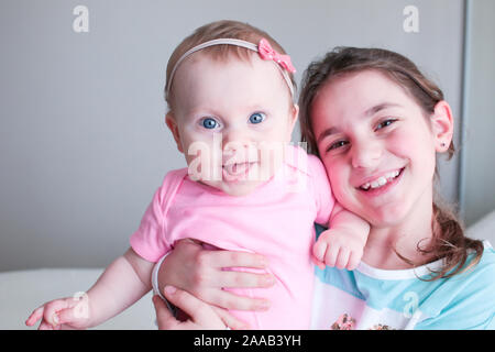 Close up ritratto di due sorelle, Cute 8 mesi ragazza con grandi occhi blu e 8 anni di età in età scolare la ragazza con occhi marroni , Happy Baby girl Foto Stock