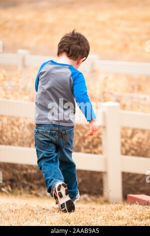 Energetic little boy in esecuzione come egli svolge nel cortile Foto Stock