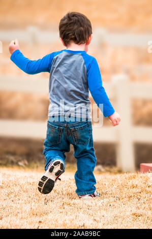 Energetic little boy in esecuzione come egli svolge nel cortile Foto Stock