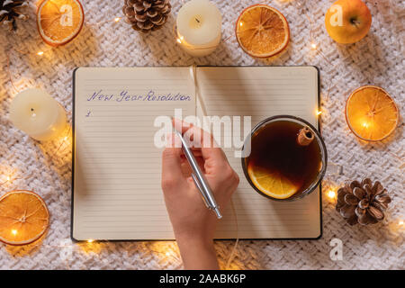 Donna mano che tiene la penna e la scrittura in notebook con tè nero e decorazioni di Natale intorno a lei Foto Stock