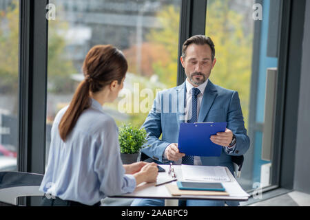 Imprenditore relazione di lettura del suo consulente finanziario mentre è seduto vicino a finestra Foto Stock