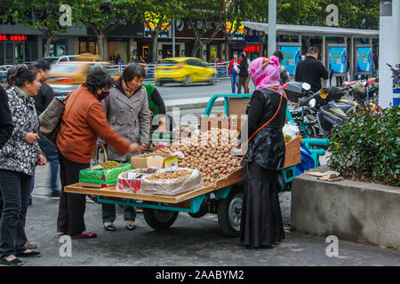 Nantong Città / Cina - Novembre 10, 2013 : Una femmina con la testa coperta la vendita di noci in strada. Sfondo sfocatura di movimento come veicoli passati. Foto Stock