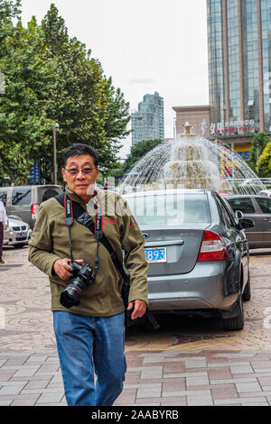 Nantong Città / Cina - 3 Ottobre 2011: uno asiatico pensionati attivo maschio passeggiate turistiche in giro in città con la fotocamera reflex digitale Foto Stock