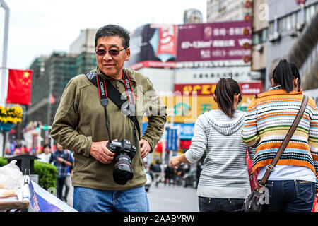 Nantong Città / Cina - 3 Ottobre 2011 : uno asiatico pensionati attivo maschio passeggiate turistiche in giro in città con la fotocamera reflex digitale Foto Stock