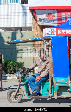 Nantong Città / Cina - Ottobre 4, 2011 : Asian uomo cinese sul riscio' elettrica, la testa girata indietro a guardare fuori per il traffico Foto Stock