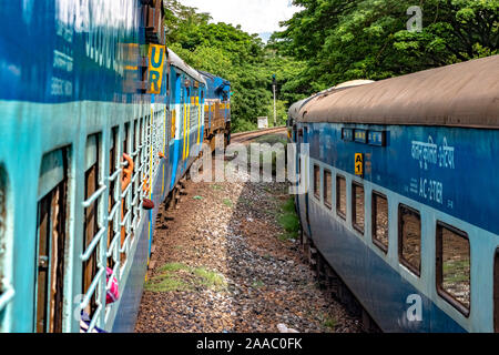 Le ferrovie indiane Treno in partenza a ritmo lento, attraversando un altro treno in esecuzione parallela ad essa in direzione opposta, immerso nel verde di i Ghati Occidentali. Foto Stock