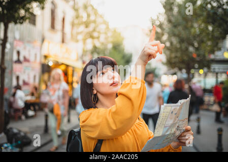 Giovane e bella ragazza in abiti alla moda con map Le passeggiate in città e si guarda intorno.Traveler Concetto di immagine Foto Stock