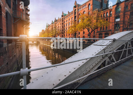 Ponte di arco su canali nella Speicherstadt di Amburgo, Germania, Europa. Storico edificio di mattoni rossi accesi da calde soft golden la luce del tramonto. Foto Stock