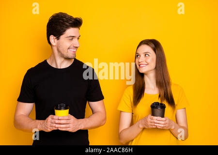 Foto di affascinanti allegro bella carino persone azienda bicchieri di carta one-off a piacere indossare nero t-shirt toothily sorridente isolato sulla vibrante shiny Foto Stock