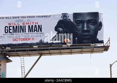 Un enorme cartellone per il film Gemini, starring Will Smith, eretta da un uomo in arancione hi viz camicia al di sopra della strada. Los Angeles, California, Stati Uniti d'America Foto Stock