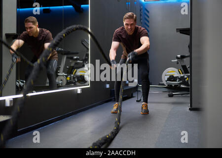 Atleta uomo in formazione con funi vicino a specchio in palestra Foto Stock