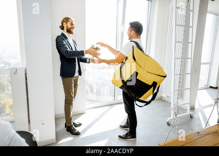 Corriere fornendo soluzioni di business lunch con borsa termica per un lavoratore di ufficio, happy businessman tenendo insalate in ufficio bianco Foto Stock