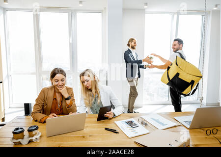 Corriere consegna sano pranzi con borsa termica per i dipendenti in sede, happy businessman tenendo insalate in ufficio bianco Foto Stock