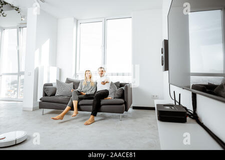 Coppia giovane rilassarsi sui comodi divani, guardare la televisione in salotto luminoso del moderno appartamento Foto Stock
