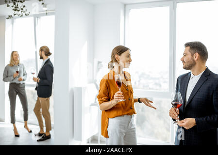 Giovani elegantemente vestito persone incontro nel corridoio bianco o showroom, parlare e bere vino durante alcuni eventi informali Foto Stock