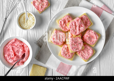 Dolce biscotti frollini e rabboccato con FRAGOLA Crema di burro alla vaniglia cosparsi di glassa commestibile con perle di argento e di cocco grattugiato su una piastra bianca Foto Stock