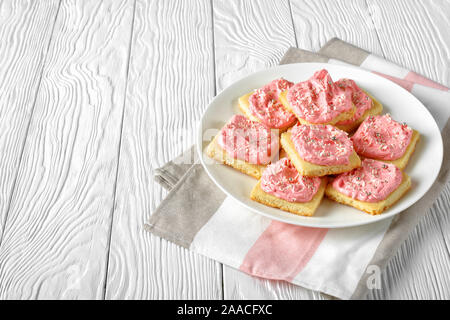 Dolce biscotti frollini e rabboccato con FRAGOLA Crema di burro alla vaniglia cosparsi di glassa commestibile con perle di argento e di cocco grattugiato su una piastra bianca, Foto Stock