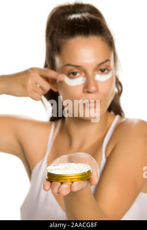 Giovane donna l'applicazione di crema per il viso sotto heer occhi su sfondo bianco Foto Stock