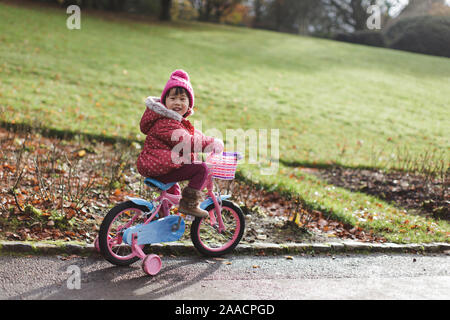 Il toddler girl bicicletta equitazione in inverno campagna parco,l'Irlanda del Nord Foto Stock