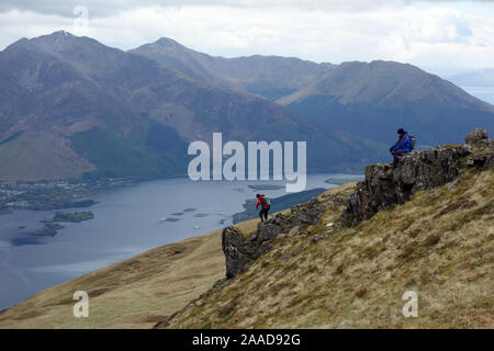 Due uomini su un promontorio roccioso sulla Corbett Mam na' Gualainn con la Munro 'Beinn un' Bheithir' in background, Highlands scozzesi, Scotland, Regno Unito. Foto Stock