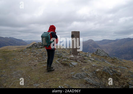 Lone Hillwalker in piedi dal calcestruzzo cilindrico punto di triangolazione sul vertice del Corbett Mam na' Gualainn, Highlands scozzesi, Scozia. Foto Stock