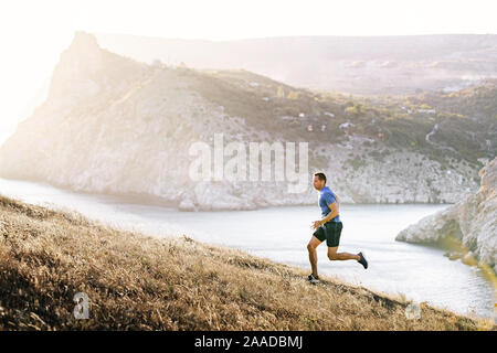 Atleta che corre in salita in tramonto sul mare di sfondo bay Foto Stock