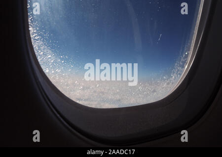 Differenza di clima al di fuori di un aereo durante la salita. Finestra congelata all'interno del velivolo ricoperta di ghiaccio durante il volo, closeup oblò vista. Foto Stock