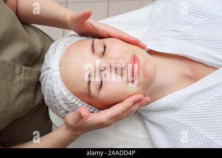 Massaggiatrice mani si muovono lentamente facendo rilassante massaggio viso alla bella ragazza client in Medical Center vista superiore Foto Stock