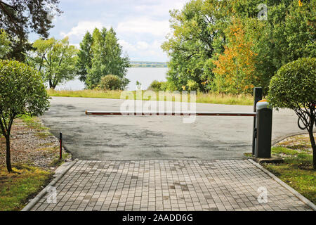 Percorso dalla pavimentazione in lastre nel parco tra pini e salici sferica e una barriera. In fondo è un lago. Foto Stock