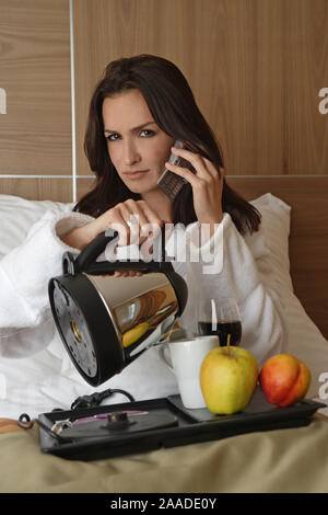 Junge muede Frau macht Fruehstueck im Bett Foto Stock