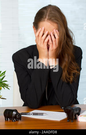 Frau sitzt mit Hände vor dem Gesicht am Schreibtisch (MR) Foto Stock