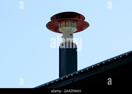 Vecchio vintage retrò rosso e bianco firehouse fatiscente siren montato sulla parte superiore della colonna di metallo sul nuovo tetto con cielo blu chiaro in background Foto Stock