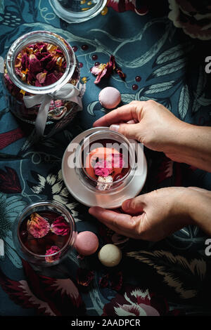 Una tazza di rosa appassita tè serviti nella donna con le mani in mano. Stato d'animo scuro flatlay Foto Stock