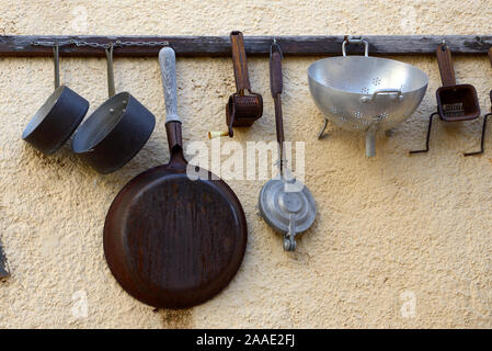 Vintage o antica collezione di vecchi utensili da cucina appeso su Rack da parete comprese pentole, drainer e Spatole Foto Stock