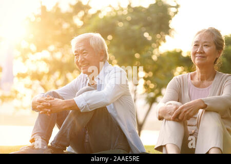 Asian senior giovane seduto sull'erba godersi il tramonto all'aperto nel parco Foto Stock