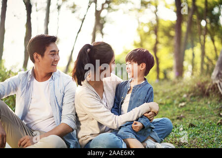 Famiglia asiatica madre padre e figlio seduti su erba rilassante avendo divertimento all'aperto nel parco Foto Stock