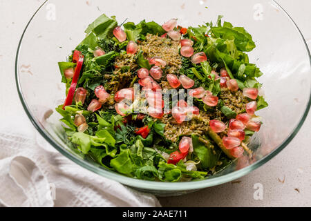 Insalata di fatti in casa con i semi di melograno e di erbe di radice di pianta salsa miscelata con due cucchiaio nella ciotola di vetro. Organici di cibi freschi. Foto Stock