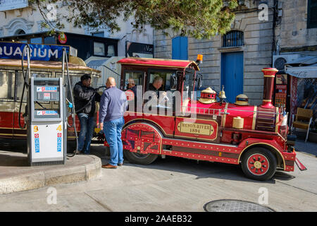 Il riempimento fino alla stazione di benzina - la strada treno che porta i turisti intorno a Mdina e Rabat in Malta Foto Stock