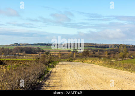 Nel tardo autunno. Verdi campi e foreste. Strada di ghiaia in primo piano. Podlasie, Polonia. Foto Stock