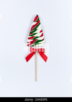 Natale Lollipop con fiocco rosso su sfondo bianco. Lecca-lecca nella forma di un albero di Natale. Vista superiore, piatto laici. Foto Stock