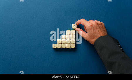 La mano di un uomo di affari di impilamento dadi di legno per formare fasi con la freccia rivolta verso l'alto in una immagine concettuale. Su sfondo blu scuro con spazio di copia Foto Stock