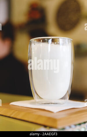 Un bicchiere di latte con pareti doppie sul tavolo di cucina per la preparazione del latte shake, cocktail di latte o caffè latte. Prodotti naturali. Foto Stock