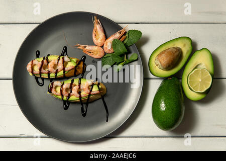 Bruschetta con gamberetti, avocado e calce su una piastra scuro su un bianco sullo sfondo di legno Foto Stock